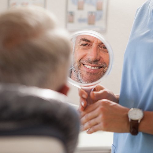 An older man looking at his new smile with a hand mirror