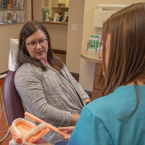 Dental team member showing proper tooth brushing technique to avoid dental emergencies