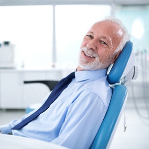 Older man in tie smiling while leaning back in dental chair