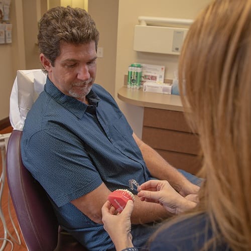 Dental team member showing patient how Invisalign tray works with smile model