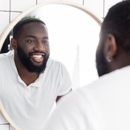 Man smiling in mirror, admiring his mini dental implant restorations