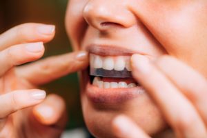 Closeup of a mouth of someone placing a whitening strip over their teeth with their fingers.